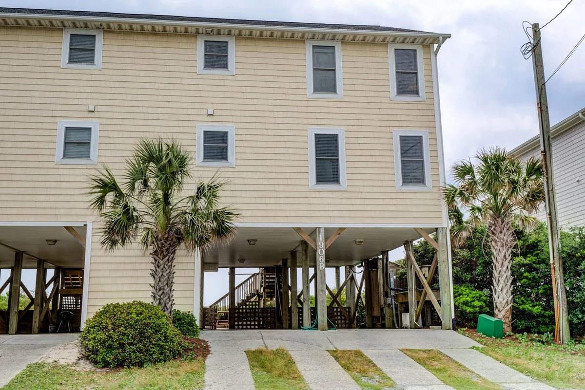 This exterior shot showcases the front entrance and porch area, framed by lush palm trees. The visible open space around the entrance suggests a welcoming, versatile outdoor area ideal for gatherings. The porch and steps hint at a home that is both family-friendly and accessible.