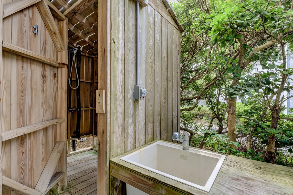This image captures a wooden outdoor shower enclosure surrounded by green landscaping, offering a blend of utility and natural beauty. The fencing and greenery create a contained, private outdoor space, enhancing the sense of a secure, multi-purpose yard.