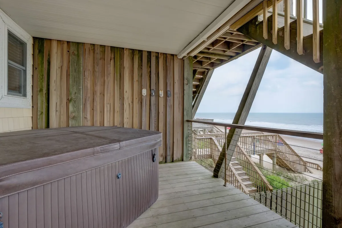 A tranquil deck scene highlighting a bubbling hot tub facing the ocean, bordered by sleek wooden railings. The composition emphasizes both the inviting water of the tub and the uninterrupted ocean vista, creating a sense of peaceful, private indulgence.