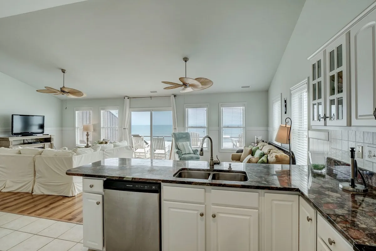 A spacious, open-plan kitchen and living area with a kitchen island, comfortable seating, and large windows revealing a breathtaking ocean view. The setup invites social interaction, cooking, entertaining, and relaxation.