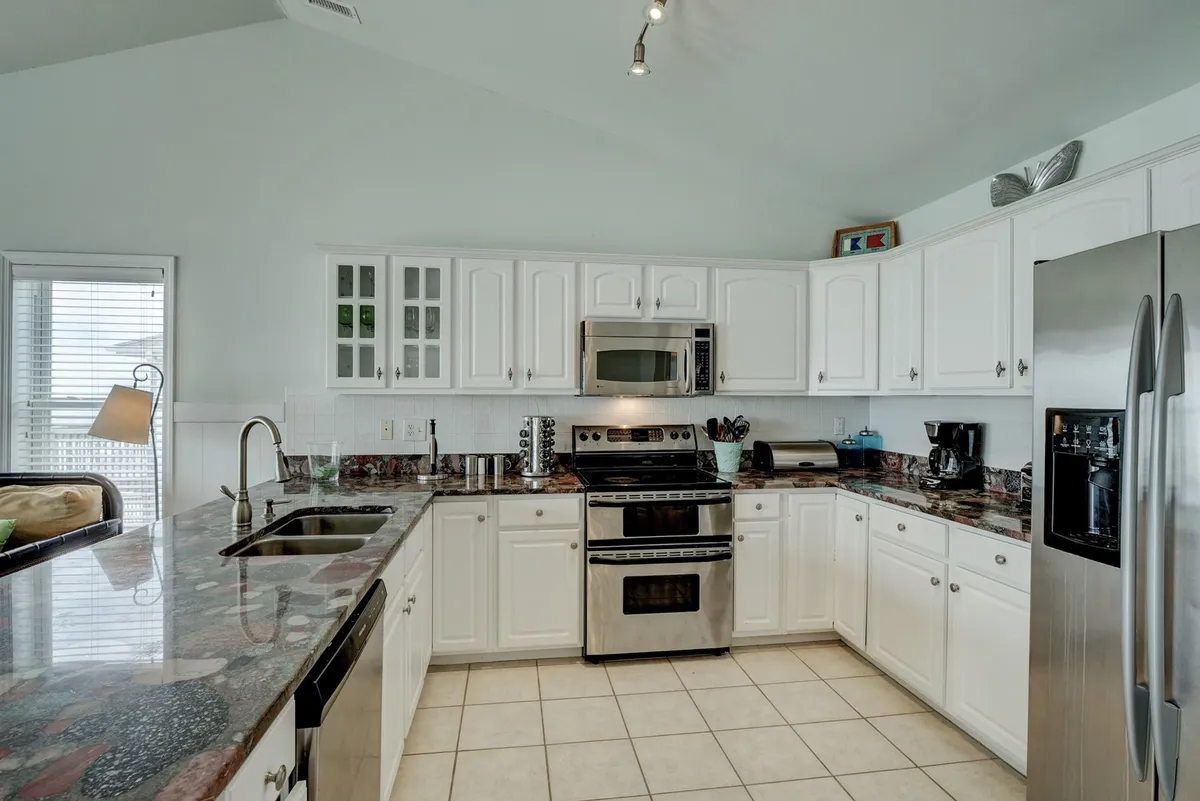 A modern kitchen is displayed with gleaming granite countertops, stainless steel appliances including a double oven, and crisp white cabinetry. The space is designed for both cooking and entertaining, providing ample counter space and an inviting atmosphere for gatherings.
