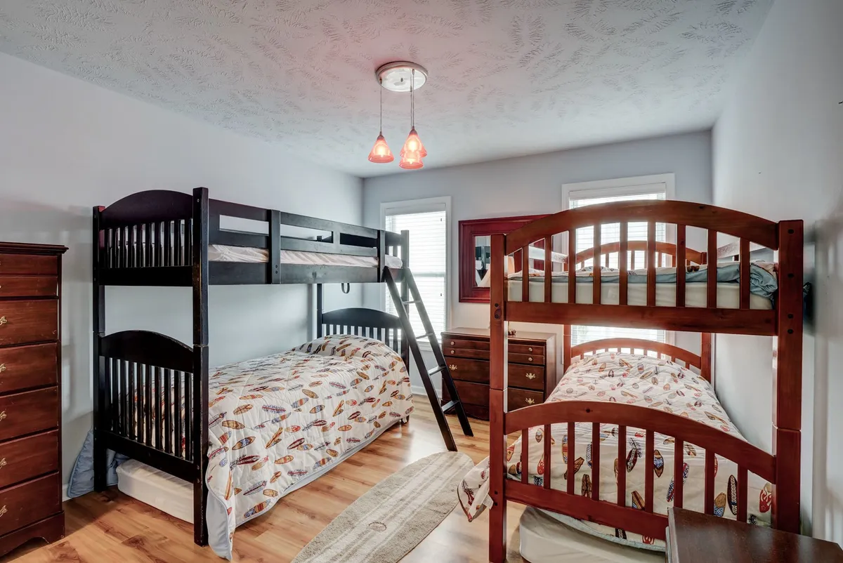 A cheerful bunk bedroom outfitted with bunk beds, a chest of drawers, a decorative rug, and playful lighting. The room is designed to appeal to children or groups, evoking a sense of fun and family togetherness.